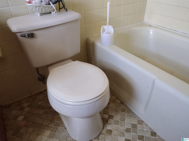 bathroom featuring a tub to relax in, toilet, and tile walls