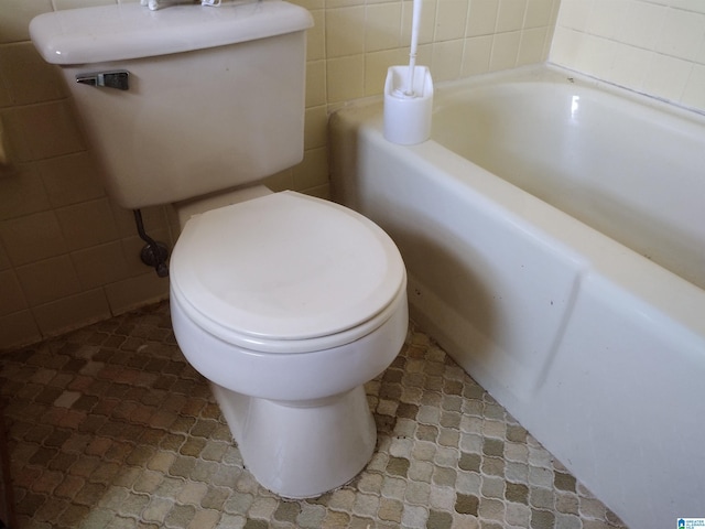 bathroom with a bath, toilet, and tile walls