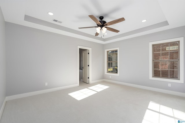 carpeted spare room with a raised ceiling and ceiling fan