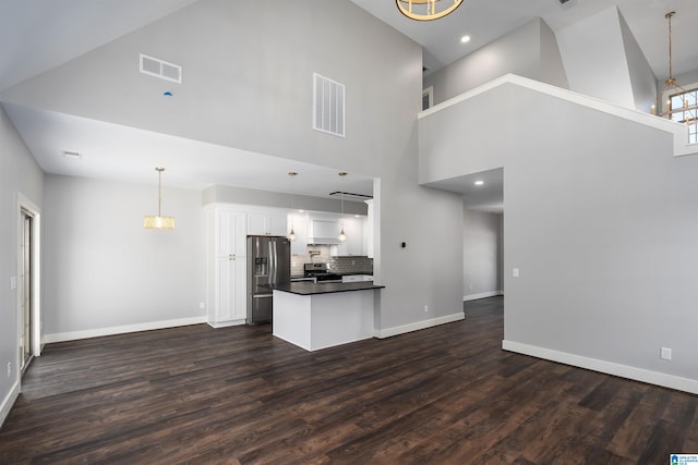 kitchen featuring a towering ceiling, white cabinets, hanging light fixtures, and appliances with stainless steel finishes