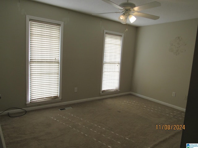 empty room featuring dark colored carpet, plenty of natural light, and ceiling fan