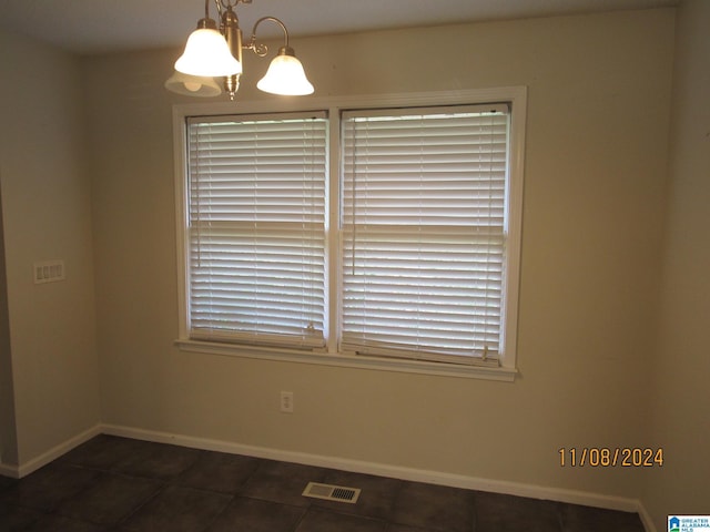 empty room with dark tile patterned flooring and an inviting chandelier