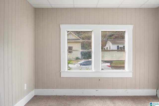 carpeted spare room with a paneled ceiling, wood walls, and a healthy amount of sunlight