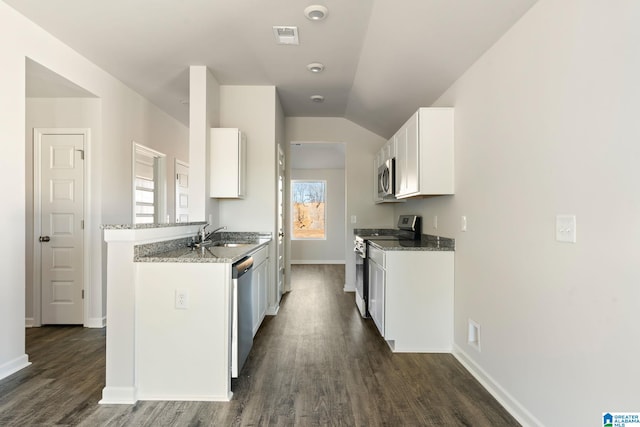 kitchen with light stone countertops, white cabinetry, stainless steel appliances, and vaulted ceiling