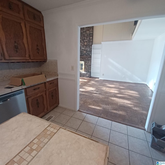 kitchen with decorative backsplash, stainless steel dishwasher, crown molding, and light tile patterned flooring