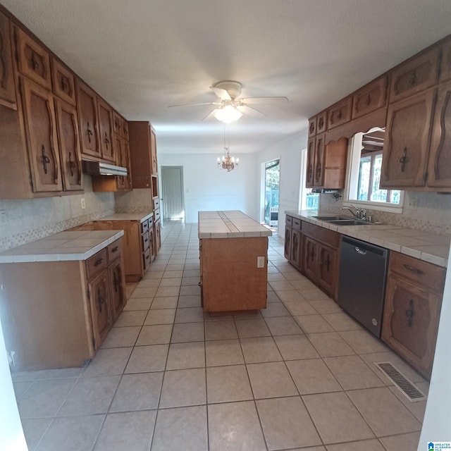 kitchen featuring a center island, ceiling fan with notable chandelier, decorative backsplash, black dishwasher, and tile counters