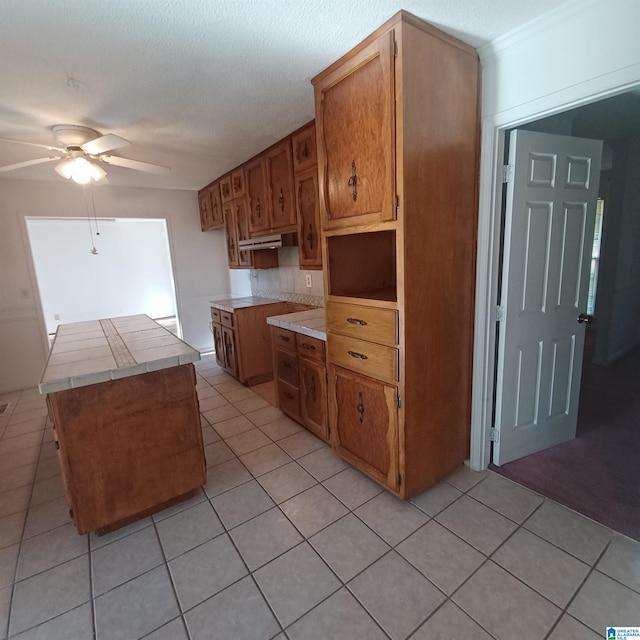 kitchen featuring a textured ceiling, ceiling fan, light tile patterned floors, tile countertops, and a center island