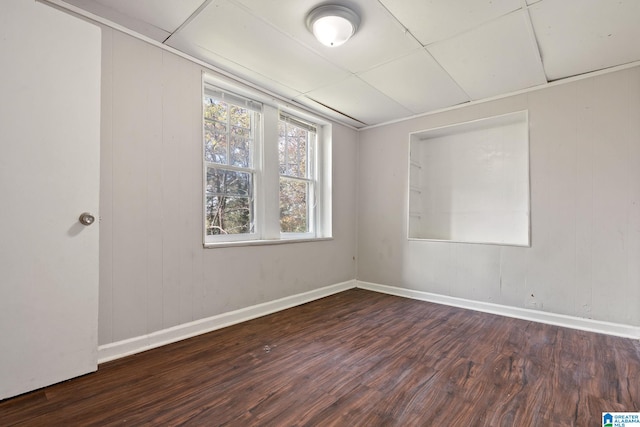 empty room featuring dark hardwood / wood-style floors, a drop ceiling, and wooden walls