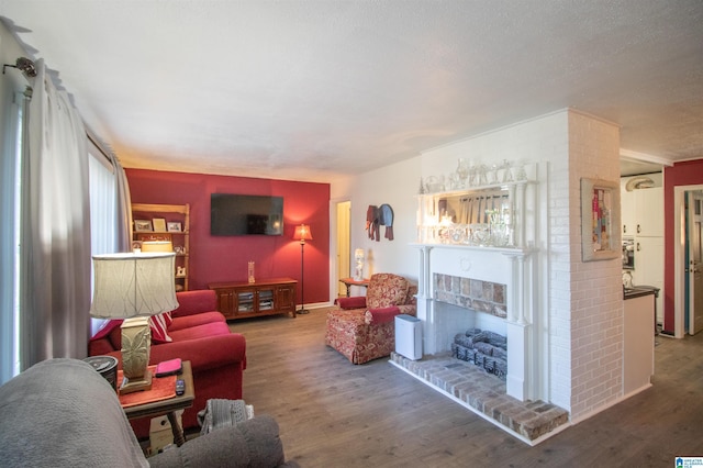 living room with wood-type flooring, a textured ceiling, a brick fireplace, and a healthy amount of sunlight