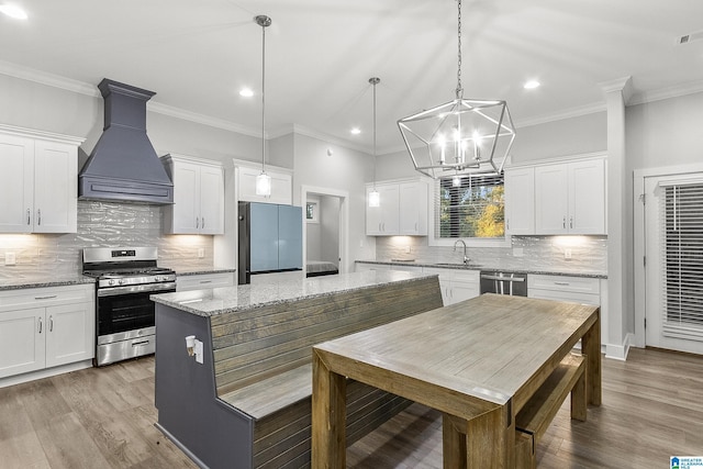 kitchen featuring custom exhaust hood, stainless steel appliances, white cabinetry, a sink, and a kitchen island