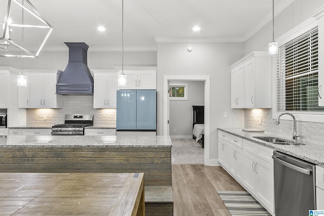 kitchen with custom exhaust hood, white cabinetry, appliances with stainless steel finishes, and a sink