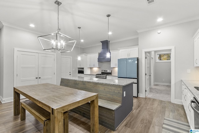 kitchen featuring decorative backsplash, wood finished floors, premium range hood, stainless steel range with gas cooktop, and white cabinetry