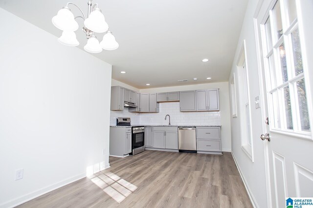 kitchen featuring appliances with stainless steel finishes, sink, decorative light fixtures, a chandelier, and light hardwood / wood-style floors