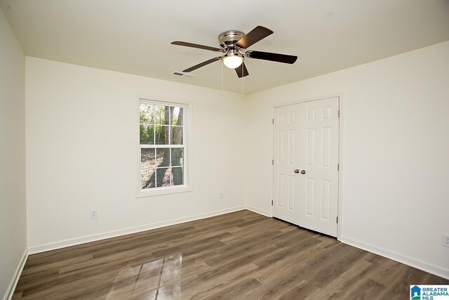 unfurnished bedroom with ceiling fan, a closet, and dark wood-type flooring