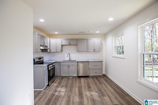 kitchen featuring hardwood / wood-style floors, gray cabinetry, sink, light stone countertops, and appliances with stainless steel finishes