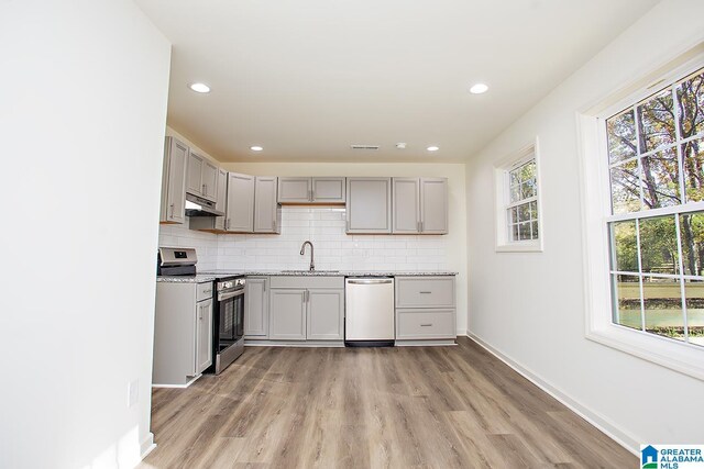 kitchen featuring appliances with stainless steel finishes, light hardwood / wood-style floors, light stone counters, and sink