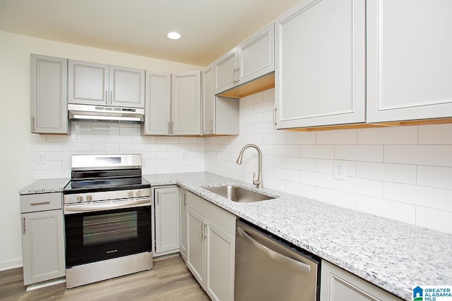 kitchen with decorative backsplash, appliances with stainless steel finishes, light stone countertops, sink, and light hardwood / wood-style floors