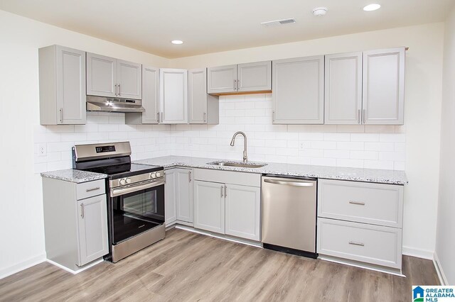 kitchen with light stone countertops, sink, stainless steel appliances, light hardwood / wood-style flooring, and backsplash