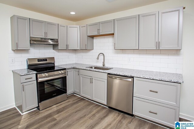 kitchen featuring backsplash, dark wood-type flooring, sink, light stone counters, and stainless steel appliances