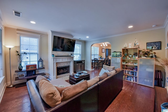 living room featuring a tiled fireplace, plenty of natural light, dark wood-type flooring, and ornamental molding