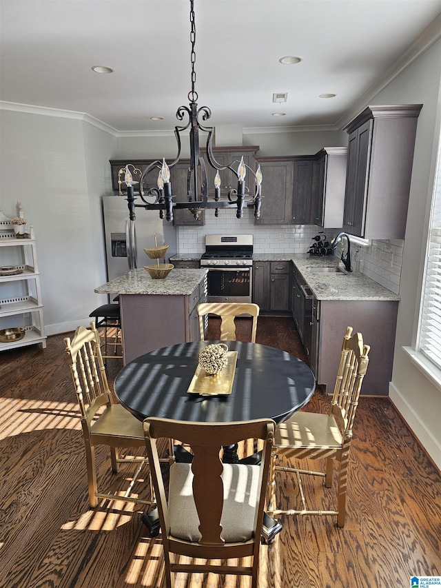 kitchen featuring a center island, dark wood-type flooring, ornamental molding, light stone counters, and stainless steel appliances