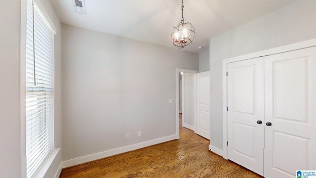 unfurnished bedroom featuring hardwood / wood-style floors, a closet, and an inviting chandelier