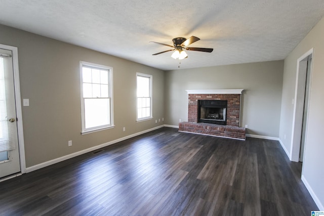 unfurnished living room featuring ceiling fan, dark hardwood / wood-style flooring, a textured ceiling, and a brick fireplace