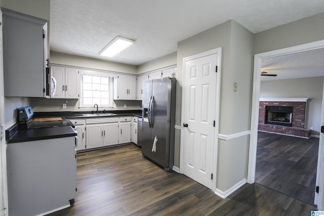 kitchen featuring sink, a brick fireplace, dark hardwood / wood-style flooring, a textured ceiling, and appliances with stainless steel finishes