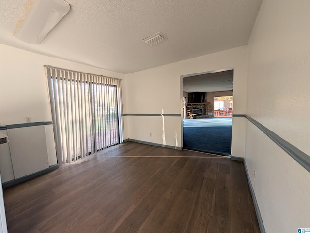 empty room featuring a textured ceiling, a fireplace, and dark hardwood / wood-style floors