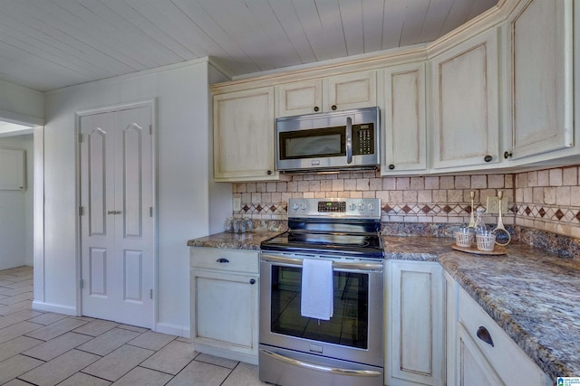 kitchen featuring decorative backsplash, cream cabinetry, stainless steel appliances, and dark stone countertops