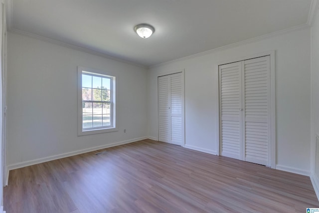 unfurnished bedroom with light hardwood / wood-style floors, crown molding, and multiple closets