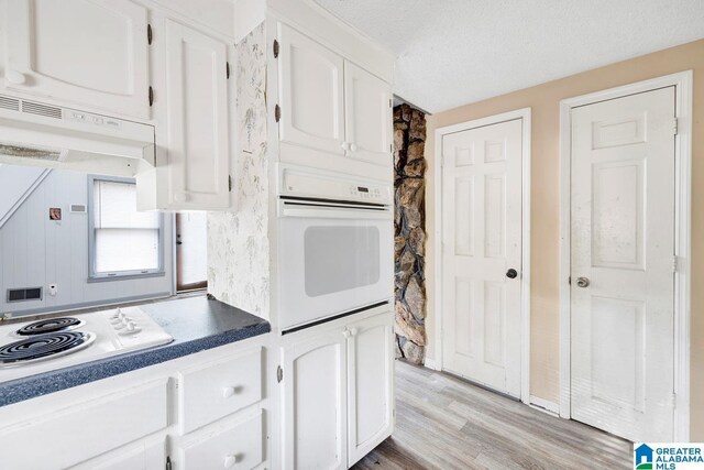 kitchen with white appliances, ventilation hood, light hardwood / wood-style flooring, a textured ceiling, and white cabinetry