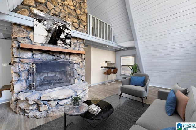 living room with hardwood / wood-style flooring, a stone fireplace, beamed ceiling, and high vaulted ceiling