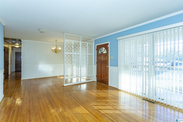 empty room featuring a notable chandelier, wood-type flooring, and crown molding