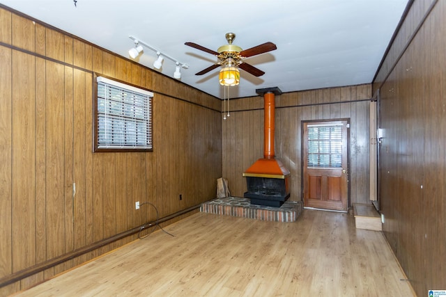 unfurnished living room featuring light hardwood / wood-style floors, ceiling fan, wood walls, and a wood stove