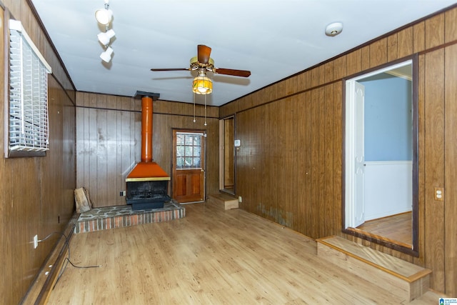 living room with light wood-type flooring, a wood stove, ceiling fan, and wood walls