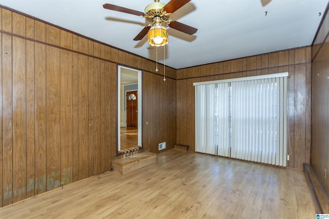 empty room featuring wooden walls, ceiling fan, and light wood-type flooring