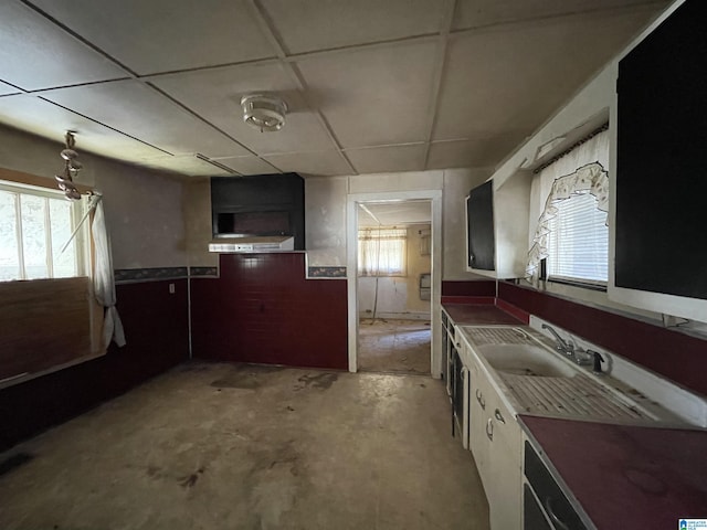 kitchen with a sink, a paneled ceiling, and unfinished concrete floors