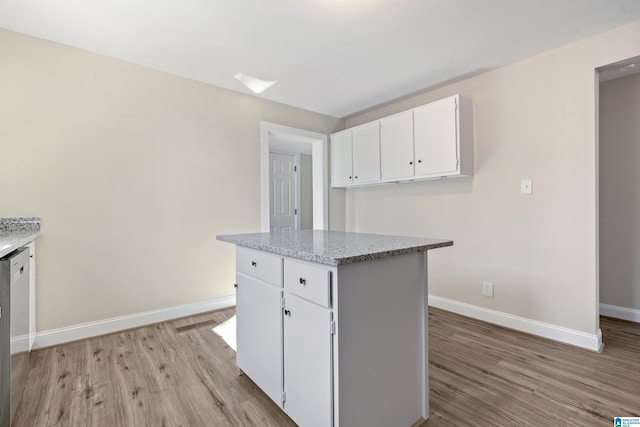 kitchen featuring white cabinetry, light stone counters, stainless steel dishwasher, light hardwood / wood-style floors, and a kitchen island