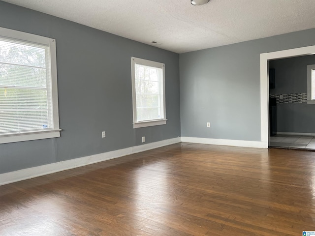 spare room with a textured ceiling, dark wood-type flooring, and a wealth of natural light