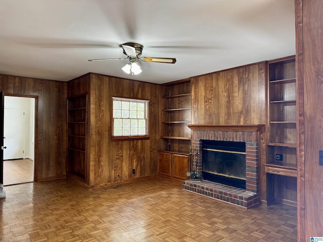 unfurnished living room featuring a fireplace, parquet floors, wooden walls, and ceiling fan