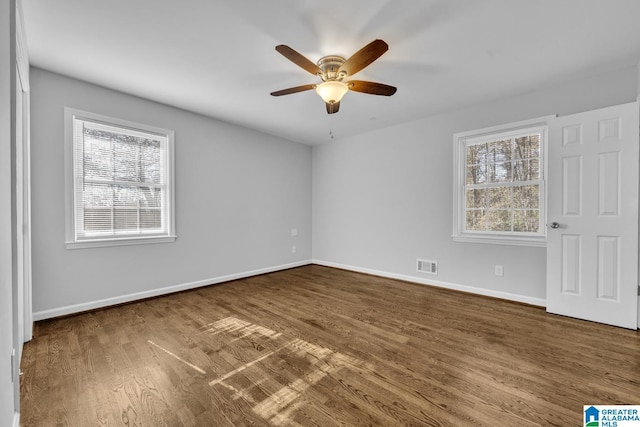 empty room featuring ceiling fan, dark wood-type flooring, and a healthy amount of sunlight