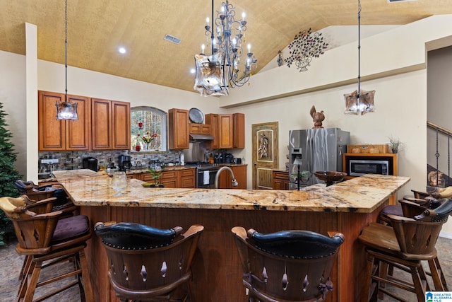 kitchen with hanging light fixtures, light stone counters, high vaulted ceiling, backsplash, and appliances with stainless steel finishes