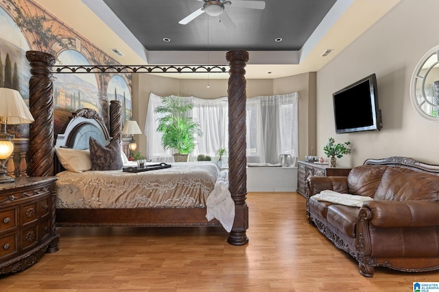 bedroom with wood-type flooring, a tray ceiling, and ceiling fan