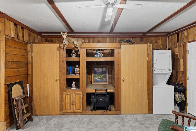 living room featuring stacked washer and clothes dryer, wooden walls, ceiling fan, a textured ceiling, and light colored carpet