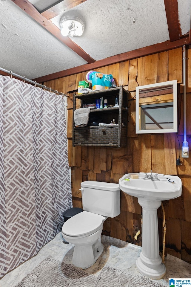 bathroom featuring a textured ceiling, toilet, and wooden walls