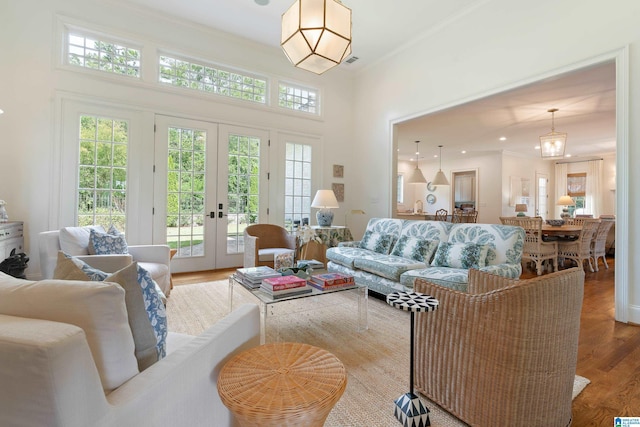 living room featuring french doors, a towering ceiling, crown molding, hardwood / wood-style flooring, and a chandelier