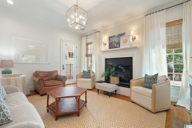 living room with crown molding, a wealth of natural light, light hardwood / wood-style flooring, and a chandelier