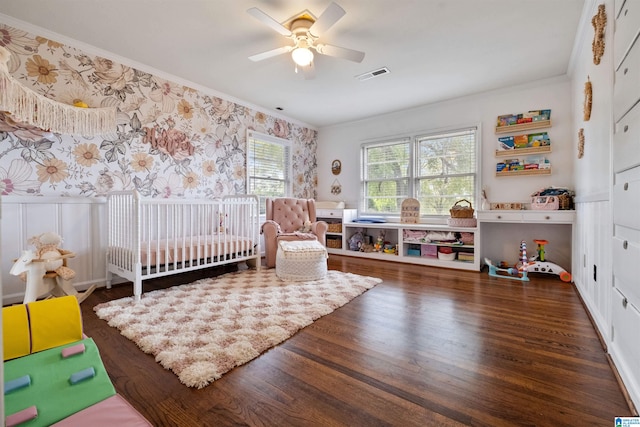 bedroom featuring ceiling fan, crown molding, dark hardwood / wood-style floors, and a crib