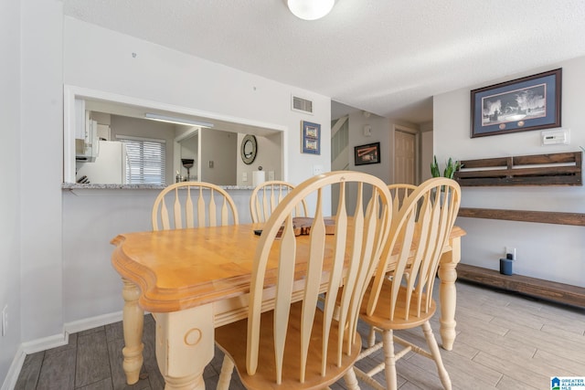 dining room with a textured ceiling and light hardwood / wood-style flooring